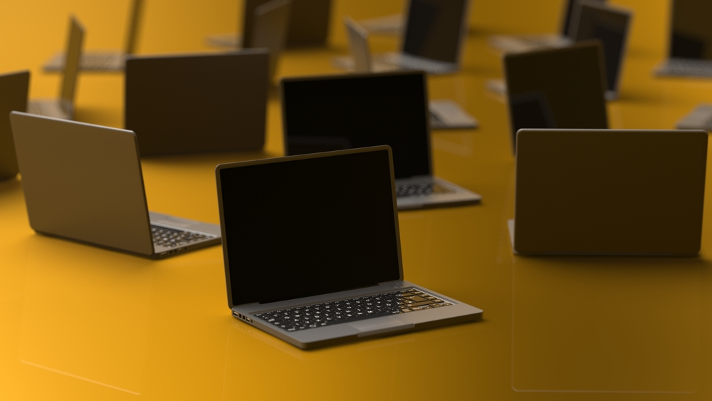 Mange laptop-er satt ut på et oransje underlag, med oransje belysning i bakgrunnen.